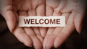 Hands gently holding a torn piece of paper with the word 'WELCOME' printed in bold brown letters.