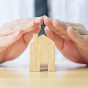 hands of health professional covering a small wooden house