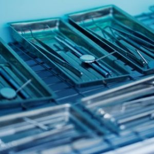 Several metal trays containing various dental instruments, such as dental mirrors, probes, and tweezers, are placed on a metal rack in a sterilization or preparation area of a dental clinic.