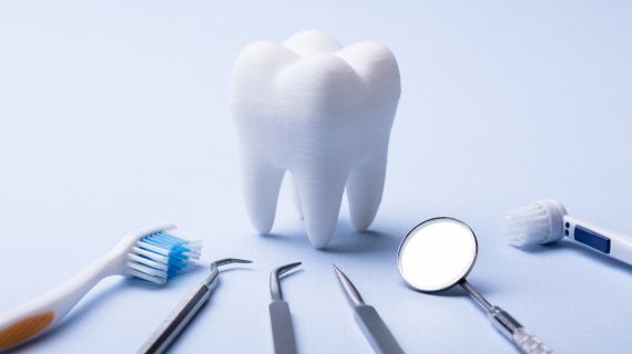 A large model of a tooth is surrounded by various dental tools on a light blue background. The tools include a toothbrush, dental explorer, tweezers, dental probe, mouth mirror, and an electric toothbrush head.